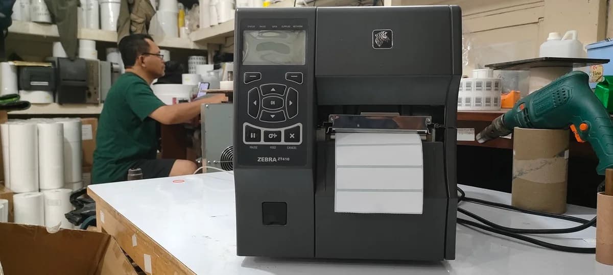 Printer thermal transfer Zebra ZT410 dengan gulungan label terpasang di meja kerja workshop