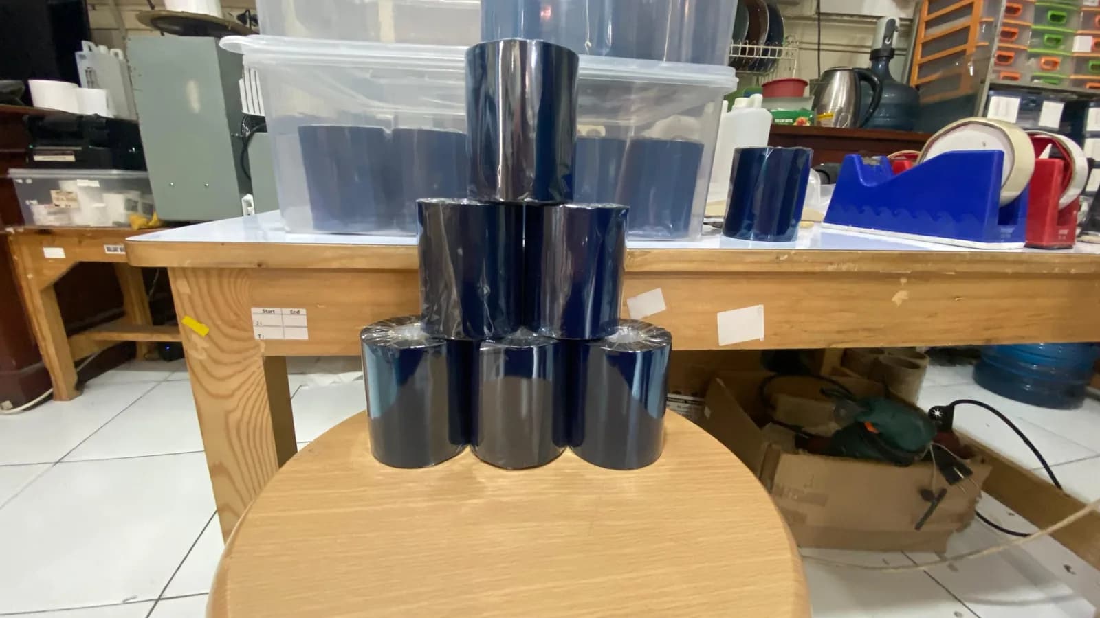 Tumpukan roll ribbon thermal transfer berwarna gelap di atas meja kerja workshop